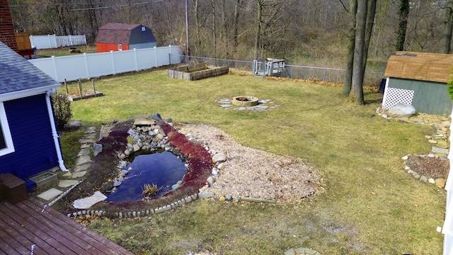 view of yard featuring an outbuilding, a garden pond, a fenced backyard, a fire pit, and a storage shed