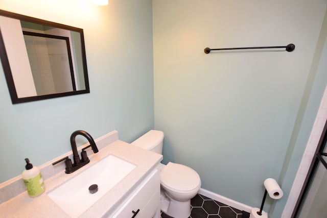 full bathroom with a tile shower, toilet, vanity, and baseboards