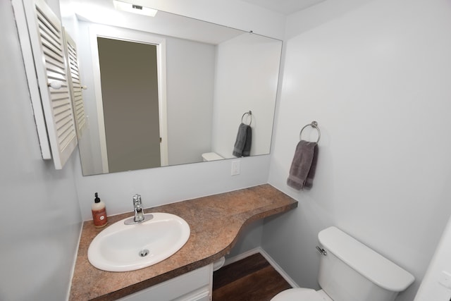 half bathroom featuring toilet, wood finished floors, and vanity