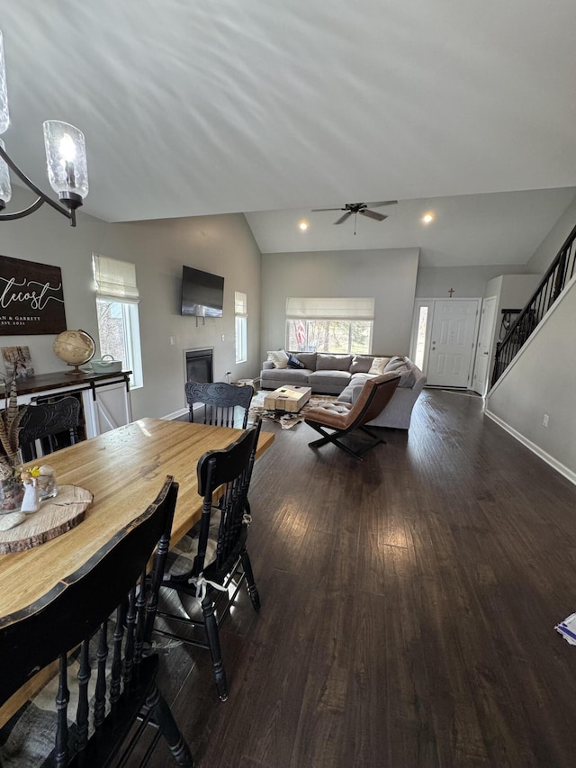 dining area with a glass covered fireplace, lofted ceiling, stairs, and wood finished floors