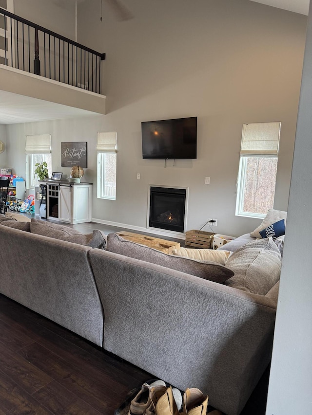 living room with dark wood finished floors, a towering ceiling, and a lit fireplace