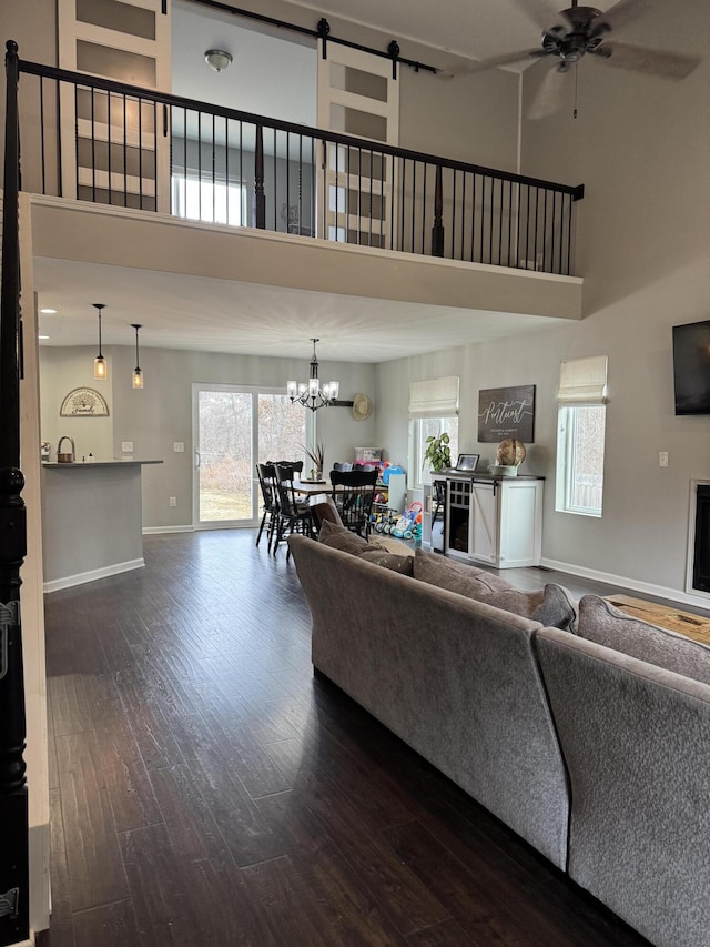 living area with baseboards, a fireplace, dark wood-type flooring, a towering ceiling, and ceiling fan with notable chandelier