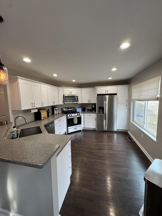 kitchen with visible vents, dark wood finished floors, appliances with stainless steel finishes, a peninsula, and a sink