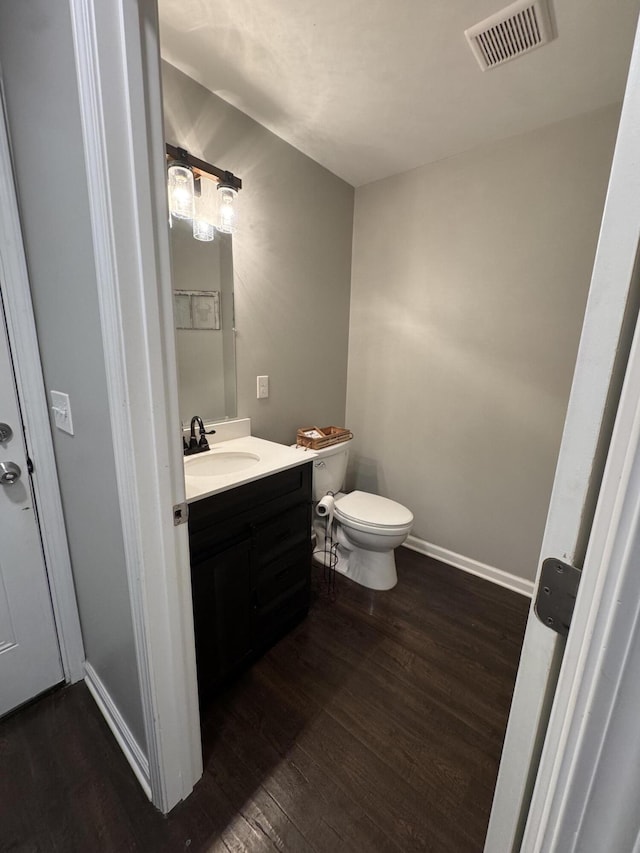 half bathroom with visible vents, vanity, baseboards, and wood finished floors