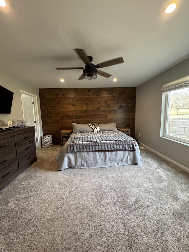 carpeted bedroom with a ceiling fan, recessed lighting, wooden walls, baseboards, and an accent wall