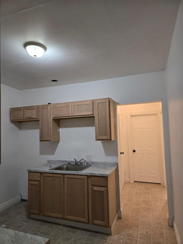 kitchen featuring light stone counters, baseboards, and a sink