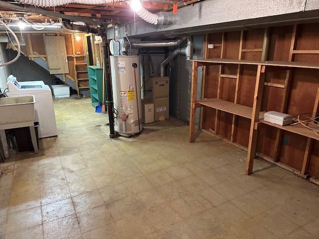 unfinished basement with gas water heater, tile patterned floors, and washer and clothes dryer