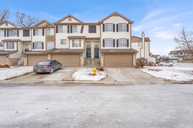 townhome / multi-family property with stone siding, an attached garage, and driveway