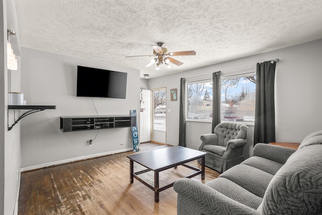 living room with a textured ceiling, wood finished floors, baseboards, and ceiling fan