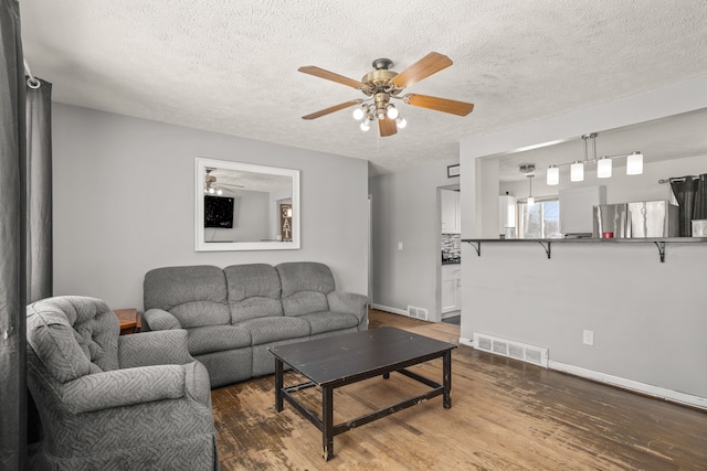 living area with visible vents, baseboards, a textured ceiling, and wood finished floors