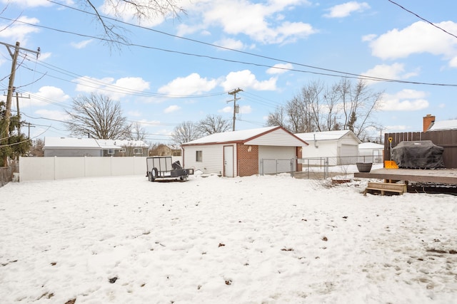 snow covered house featuring an outbuilding, a fenced backyard, and a garage