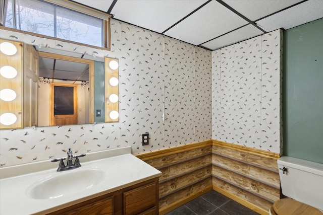 bathroom with wallpapered walls, a drop ceiling, toilet, tile patterned floors, and vanity