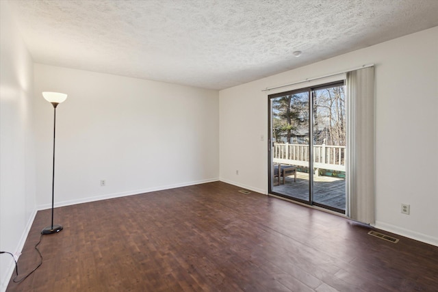 empty room featuring a textured ceiling, wood finished floors, visible vents, and baseboards