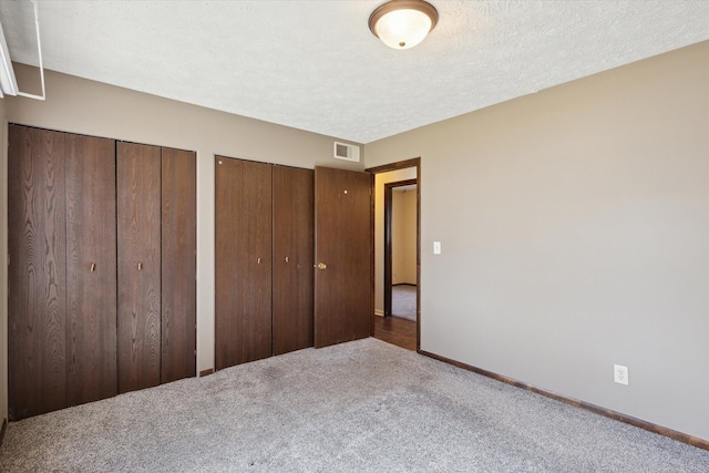 unfurnished bedroom with visible vents, baseboards, multiple closets, carpet floors, and a textured ceiling