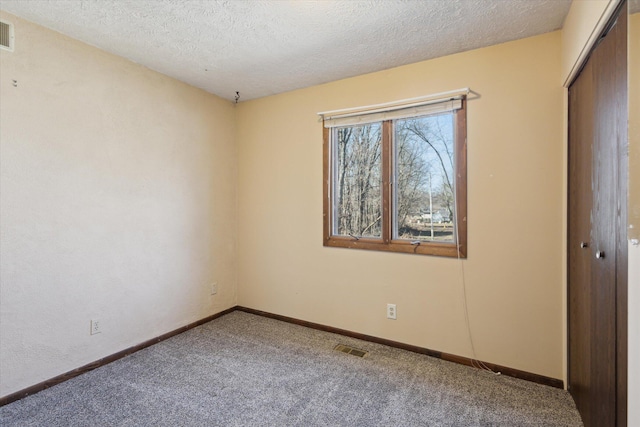 carpeted empty room featuring visible vents, a textured ceiling, and baseboards