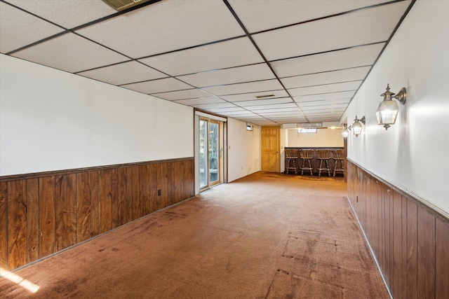 carpeted spare room with a wainscoted wall, wooden walls, and a bar