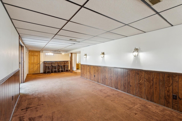 interior space featuring a wainscoted wall, carpet floors, a paneled ceiling, wood walls, and a dry bar