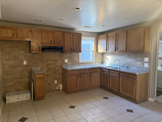 kitchen featuring brown cabinetry, visible vents, under cabinet range hood, and a sink