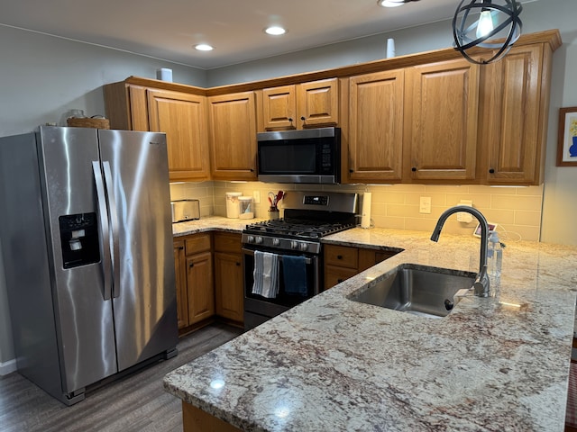 kitchen featuring light stone countertops, brown cabinetry, a peninsula, a sink, and appliances with stainless steel finishes