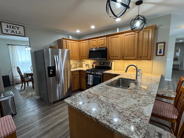 kitchen with a peninsula, light stone counters, appliances with stainless steel finishes, and a sink