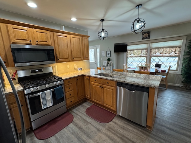 kitchen featuring a peninsula, a sink, decorative backsplash, dark wood-type flooring, and appliances with stainless steel finishes