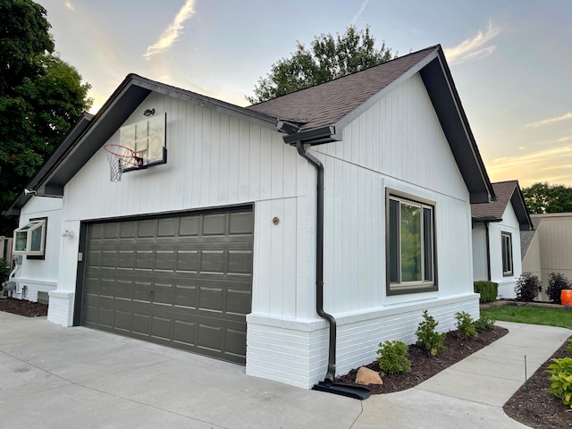 property exterior at dusk with an attached garage, concrete driveway, and roof with shingles