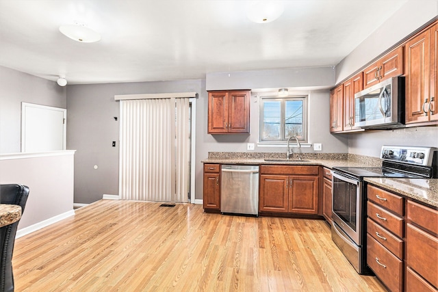 kitchen featuring a sink, brown cabinets, light wood finished floors, and stainless steel appliances