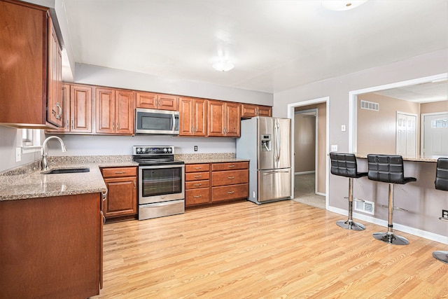 kitchen featuring visible vents, a sink, light stone counters, stainless steel appliances, and brown cabinetry