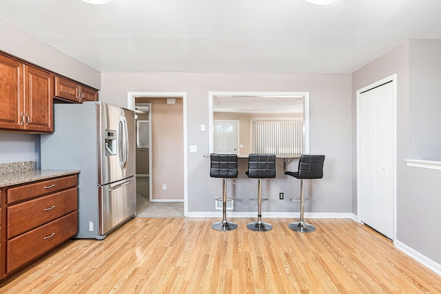 kitchen featuring light wood-type flooring, visible vents, stainless steel fridge, brown cabinetry, and baseboards