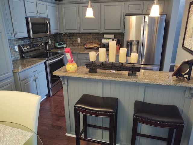 kitchen with dark wood-type flooring, gray cabinetry, tasteful backsplash, stainless steel appliances, and a breakfast bar area