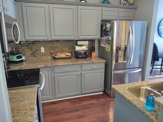 kitchen with light stone counters, decorative backsplash, appliances with stainless steel finishes, and dark wood-style flooring