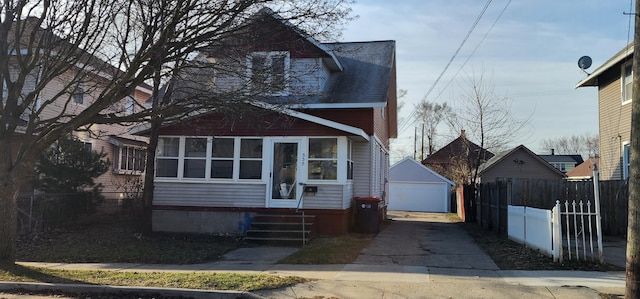 view of front facade with an outbuilding, entry steps, a detached garage, fence, and roof with shingles