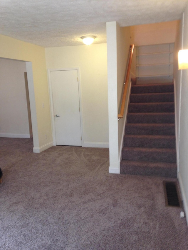 below grade area featuring visible vents, a textured ceiling, carpet flooring, baseboards, and stairs