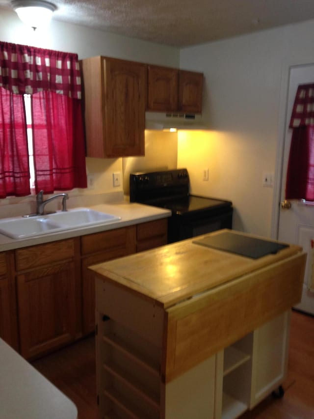 kitchen featuring a sink, under cabinet range hood, black electric range oven, brown cabinets, and a center island