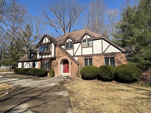 tudor house with brick siding, stucco siding, driveway, and a shingled roof