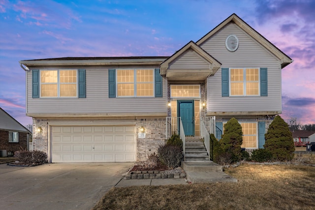 raised ranch featuring a garage, brick siding, central AC, and driveway