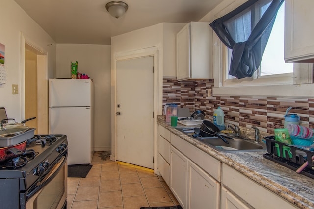 kitchen featuring a sink, backsplash, black gas stove, white cabinetry, and freestanding refrigerator