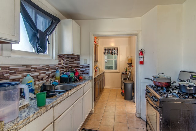 kitchen featuring light tile patterned floors, a sink, white cabinets, stainless steel gas range oven, and tasteful backsplash