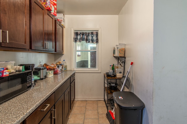 kitchen with light tile patterned floors, stone counters, baseboards, and black microwave