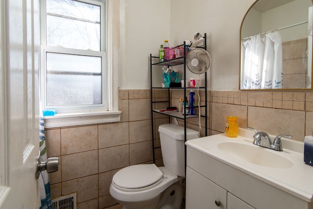 bathroom featuring visible vents, tile walls, a wainscoted wall, toilet, and vanity