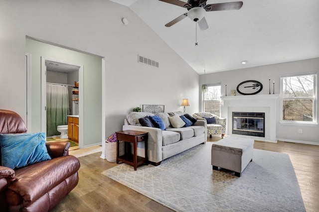 living area with visible vents, light wood-style flooring, high vaulted ceiling, and a glass covered fireplace