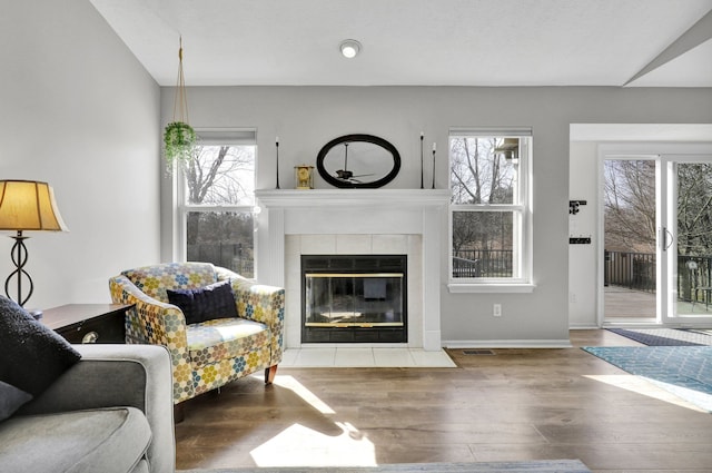 living room with a tiled fireplace, visible vents, a wealth of natural light, and wood finished floors