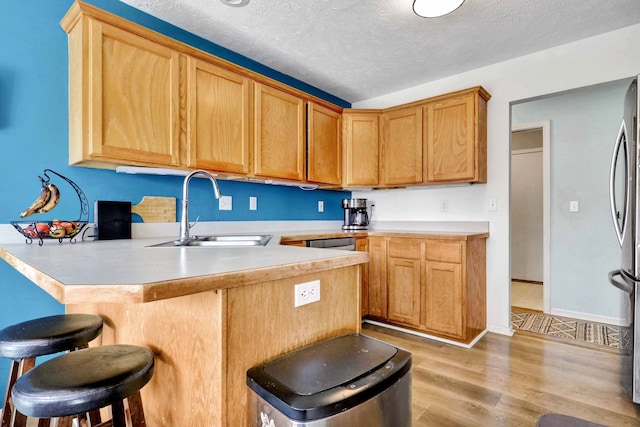 kitchen featuring light wood finished floors, a sink, a peninsula, a breakfast bar area, and light countertops