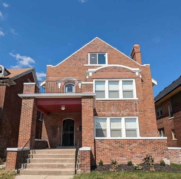 view of front of house with brick siding, covered porch, and a chimney