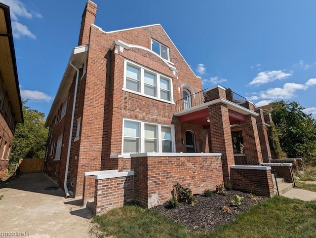 view of front of home featuring brick siding, a chimney, a balcony, and fence