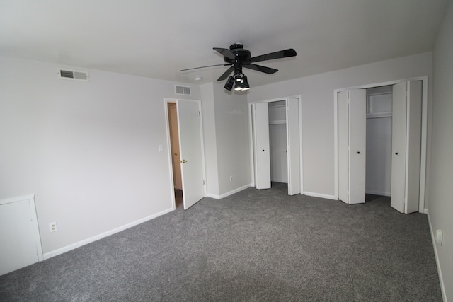 unfurnished bedroom featuring visible vents, multiple closets, baseboards, and dark carpet