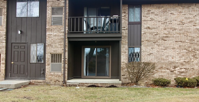 view of exterior entry with board and batten siding, a balcony, and brick siding