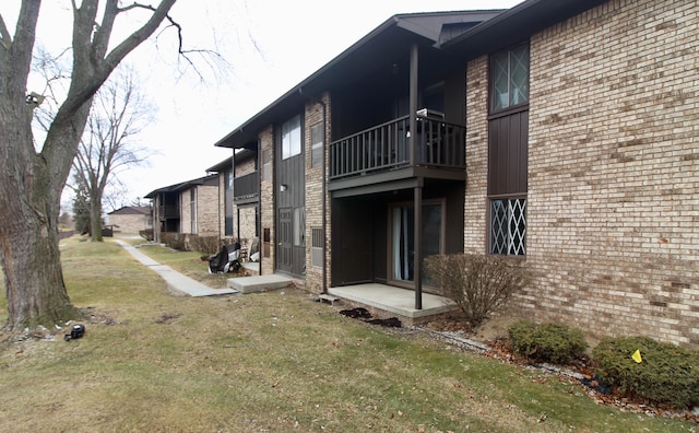 view of property exterior with brick siding, a balcony, and a yard