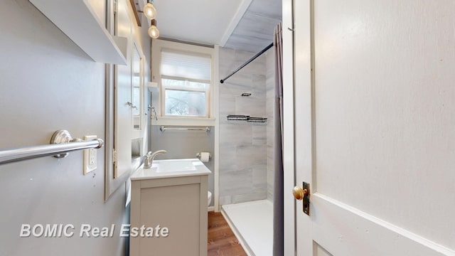 bathroom featuring toilet, wood finished floors, vanity, and a tile shower