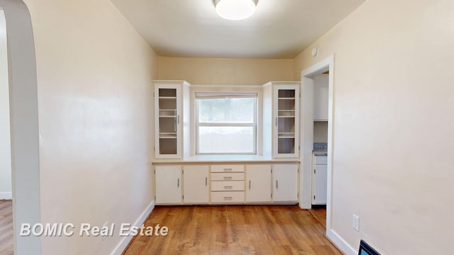 unfurnished office featuring a baseboard heating unit, light wood-style floors, arched walkways, and baseboards